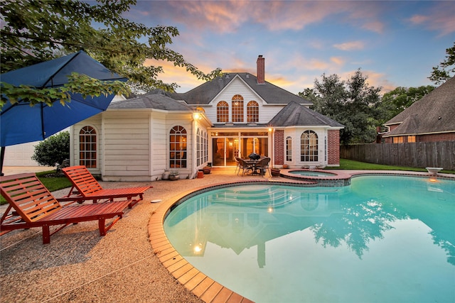 back house at dusk with a pool with hot tub and a patio area