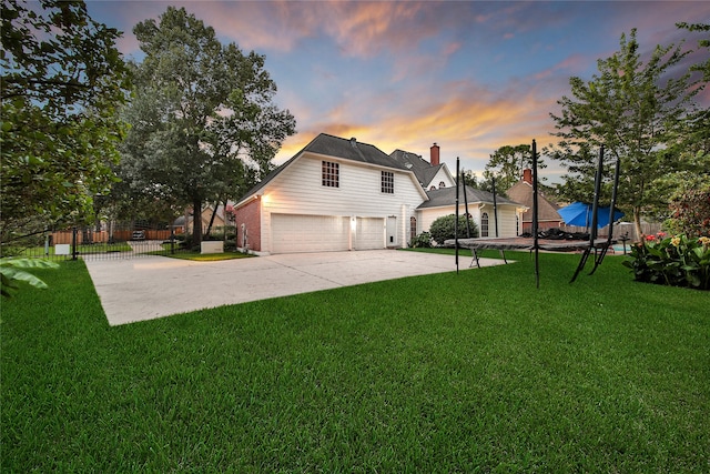 property exterior at dusk with a garage, a trampoline, and a lawn