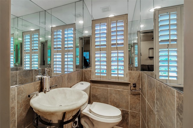 bathroom featuring toilet, tile walls, and sink