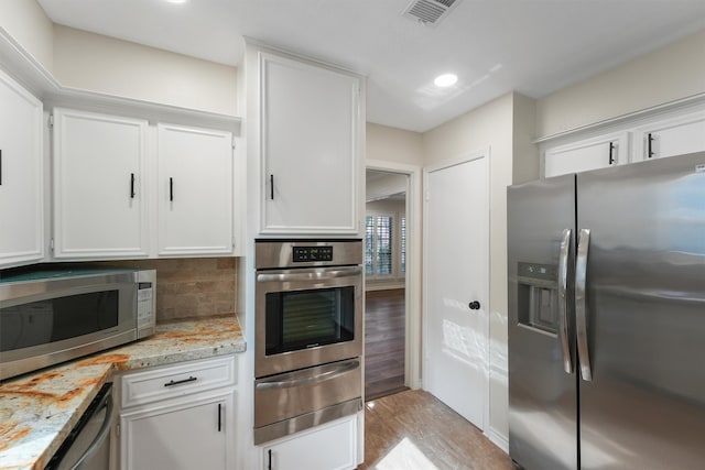 kitchen with white cabinets, appliances with stainless steel finishes, light hardwood / wood-style flooring, and light stone counters