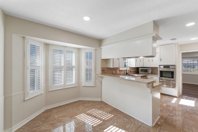 kitchen featuring white cabinets, a healthy amount of sunlight, kitchen peninsula, and appliances with stainless steel finishes