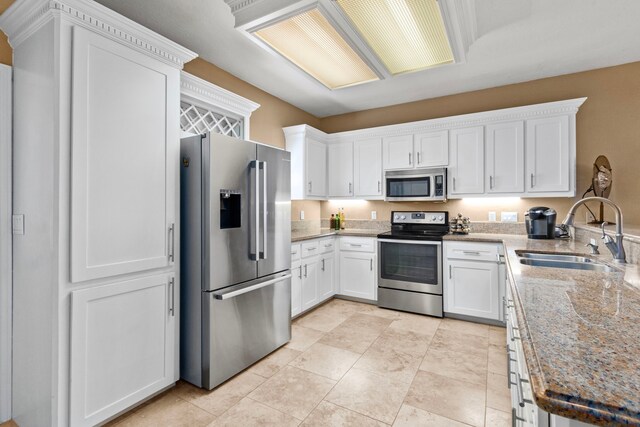 kitchen with light stone counters, stainless steel appliances, sink, and white cabinets