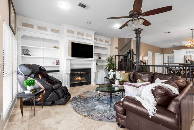 tiled living room featuring ceiling fan with notable chandelier, built in features, and a tile fireplace