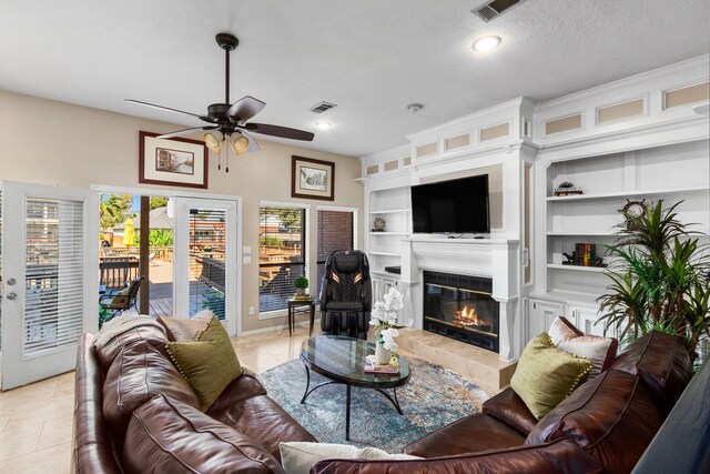 living room featuring light tile patterned floors, built in features, ceiling fan, a fireplace, and a textured ceiling