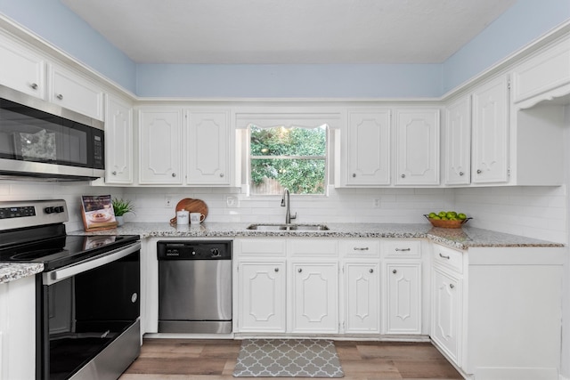 kitchen with sink, appliances with stainless steel finishes, light stone countertops, white cabinets, and dark wood-type flooring