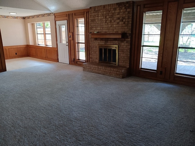 unfurnished living room with carpet flooring, wood walls, a textured ceiling, and a brick fireplace