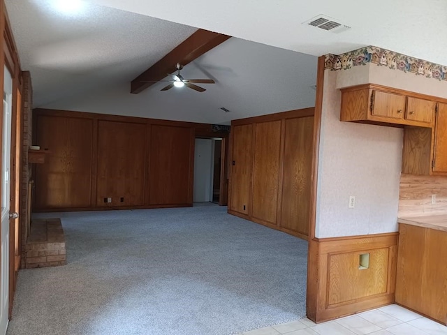 unfurnished living room with wood walls, lofted ceiling with beams, ceiling fan, and light colored carpet