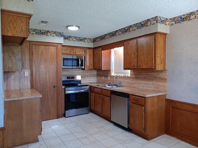 kitchen with sink, stainless steel appliances, tasteful backsplash, a textured ceiling, and light tile patterned flooring