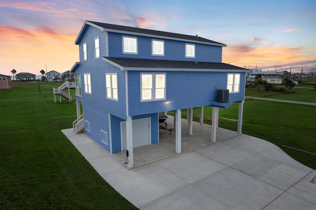 back house at dusk with central air condition unit, a garage, a yard, and a carport