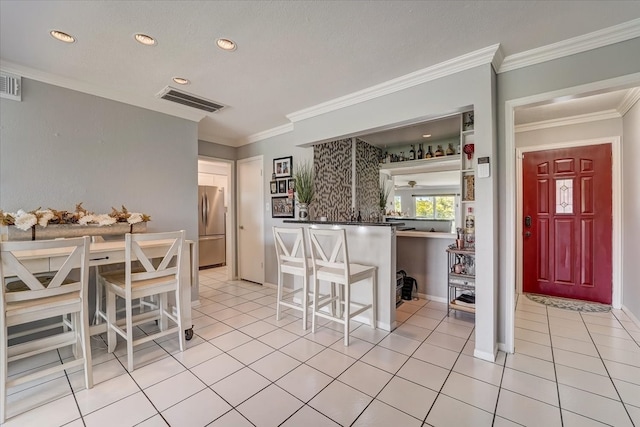 kitchen featuring a kitchen bar, kitchen peninsula, light tile patterned floors, ornamental molding, and stainless steel fridge