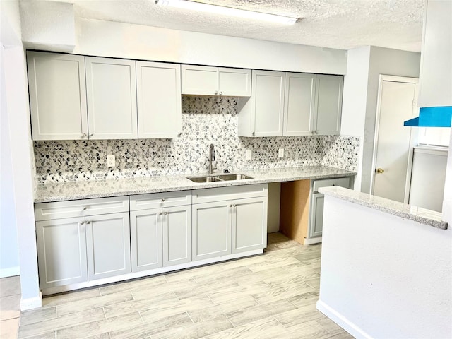 kitchen featuring light stone countertops, sink, light hardwood / wood-style floors, a textured ceiling, and decorative backsplash