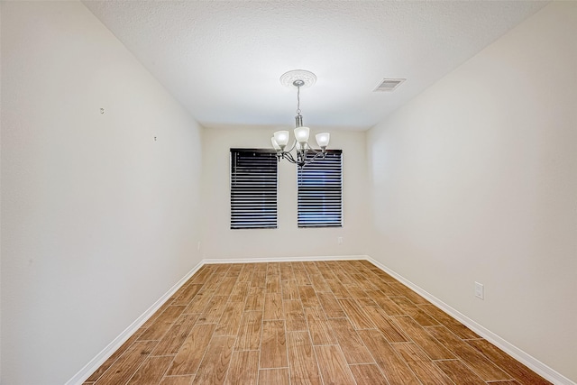 spare room with hardwood / wood-style floors, a textured ceiling, and an inviting chandelier