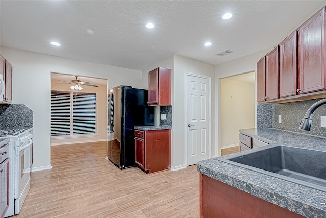 kitchen featuring decorative backsplash, stainless steel fridge, light hardwood / wood-style floors, and white gas range oven