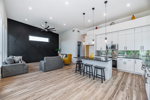 kitchen featuring appliances with stainless steel finishes, decorative light fixtures, a kitchen bar, white cabinets, and light hardwood / wood-style flooring