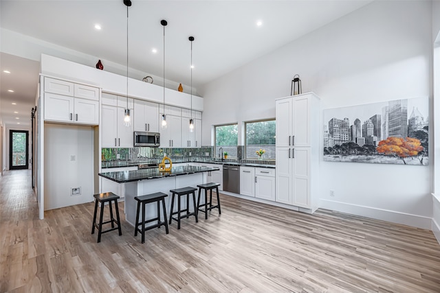 kitchen featuring light hardwood / wood-style floors, a kitchen island, white cabinetry, appliances with stainless steel finishes, and decorative light fixtures