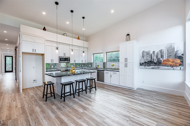 kitchen with stainless steel appliances, white cabinets, a kitchen island, pendant lighting, and light hardwood / wood-style flooring