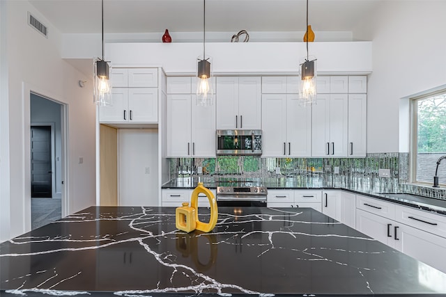 kitchen featuring stainless steel appliances, dark stone counters, backsplash, white cabinets, and pendant lighting