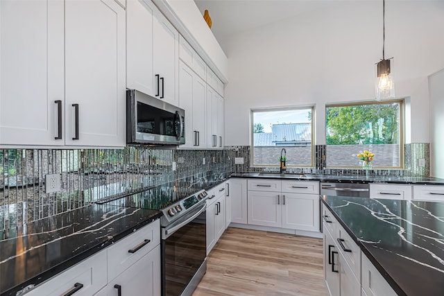 kitchen featuring white cabinetry, appliances with stainless steel finishes, sink, dark stone countertops, and light hardwood / wood-style flooring