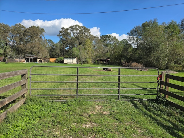 view of gate with a storage shed, a rural view, and a yard