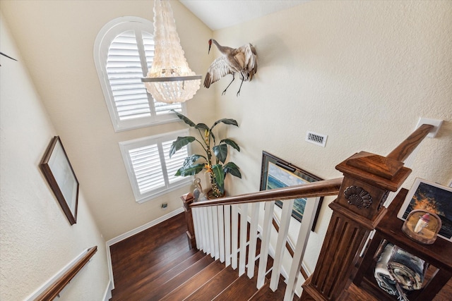 stairway featuring an inviting chandelier, hardwood / wood-style flooring, and a towering ceiling