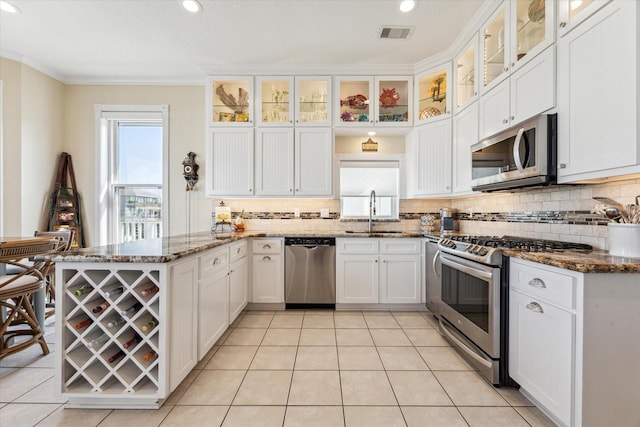 kitchen featuring sink, appliances with stainless steel finishes, dark stone countertops, white cabinetry, and backsplash