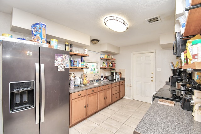 kitchen featuring sink, light tile patterned floors, stainless steel fridge, and a textured ceiling