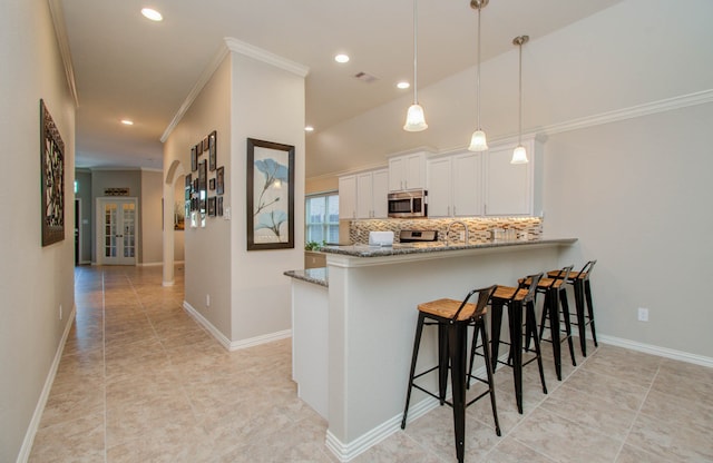 kitchen featuring appliances with stainless steel finishes, decorative light fixtures, light stone countertops, white cabinets, and kitchen peninsula