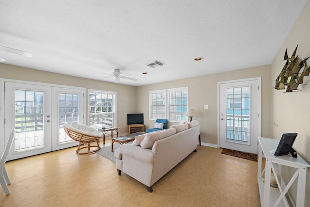 living room with ceiling fan, a textured ceiling, light hardwood / wood-style flooring, and french doors