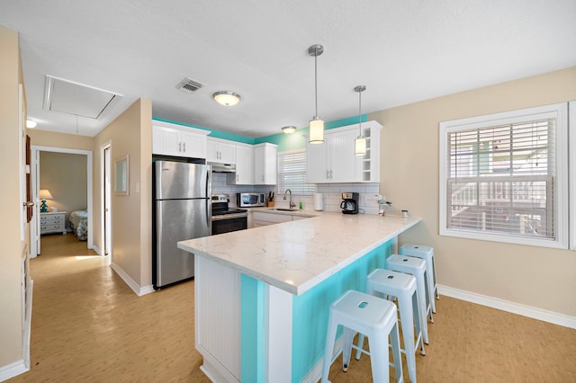 kitchen with stainless steel appliances, light hardwood / wood-style floors, backsplash, white cabinets, and pendant lighting