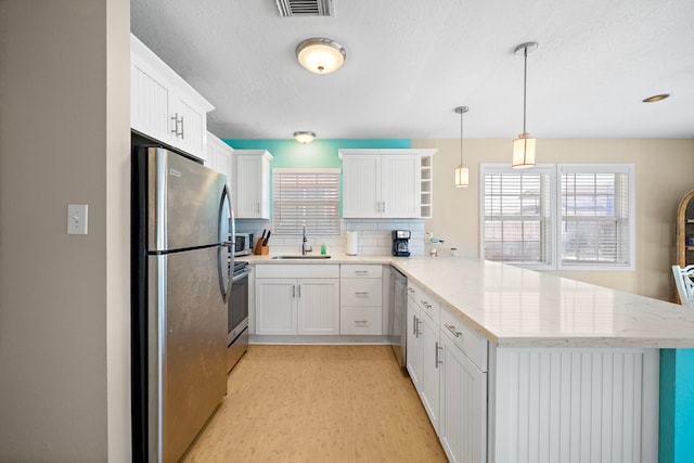 kitchen with white cabinets, kitchen peninsula, sink, appliances with stainless steel finishes, and decorative light fixtures