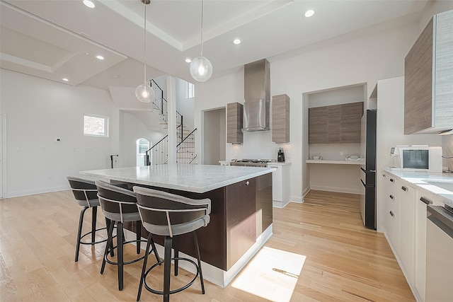 kitchen featuring pendant lighting, appliances with stainless steel finishes, light hardwood / wood-style floors, a kitchen island, and wall chimney exhaust hood