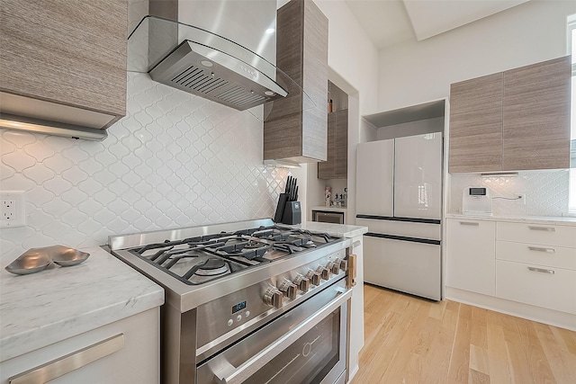 kitchen featuring decorative backsplash, white fridge, stainless steel range, wall chimney exhaust hood, and light hardwood / wood-style flooring