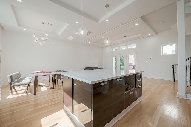 kitchen with a spacious island, dark brown cabinets, light wood-type flooring, a raised ceiling, and pendant lighting