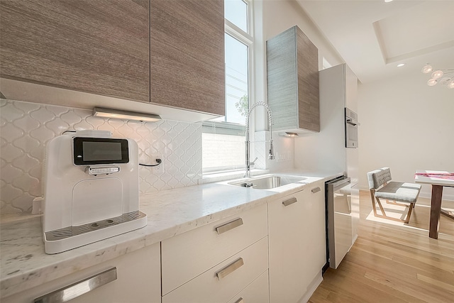 kitchen featuring sink, light stone counters, tasteful backsplash, light wood-type flooring, and dishwasher