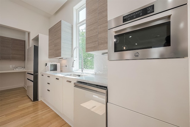 kitchen with white cabinetry, sink, light stone counters, light hardwood / wood-style floors, and stainless steel appliances