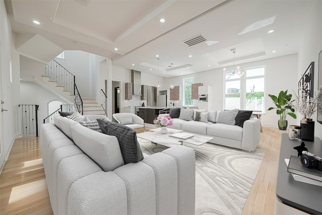 living room with an inviting chandelier, a tray ceiling, and light wood-type flooring