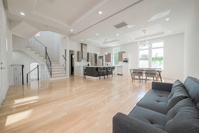 living room with an inviting chandelier, a tray ceiling, light hardwood / wood-style floors, and a high ceiling