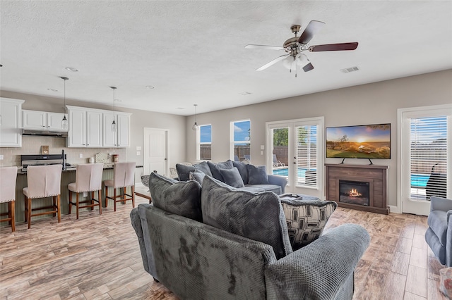 living room featuring a textured ceiling, light hardwood / wood-style flooring, and ceiling fan