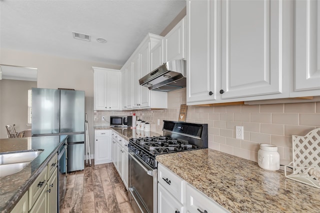 kitchen featuring appliances with stainless steel finishes, light stone countertops, white cabinets, light wood-type flooring, and decorative backsplash