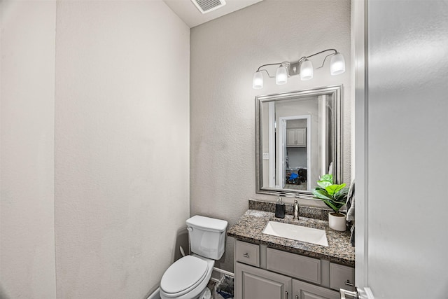 bathroom featuring visible vents, a textured wall, toilet, vanity, and baseboards