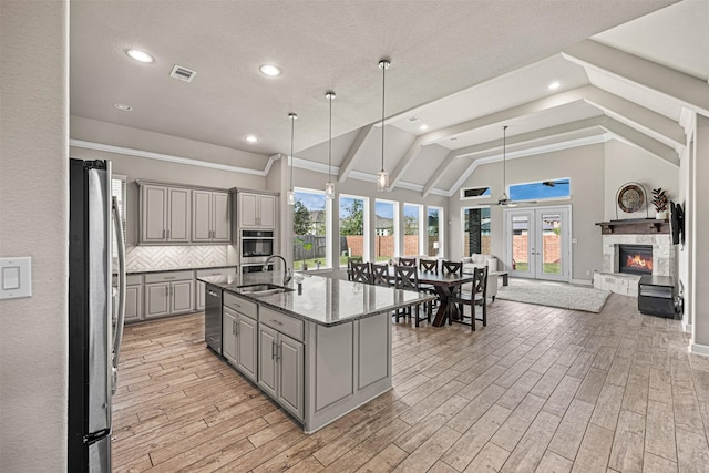 kitchen featuring gray cabinetry, a sink, open floor plan, appliances with stainless steel finishes, and decorative backsplash