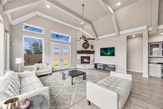 living area with high vaulted ceiling, a fireplace, baseboards, french doors, and light wood finished floors