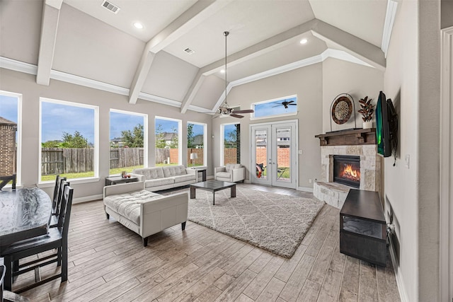 living area featuring baseboards, visible vents, wood finished floors, a stone fireplace, and high vaulted ceiling