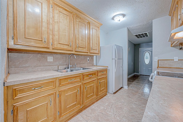 kitchen with a textured ceiling, sink, backsplash, and white refrigerator