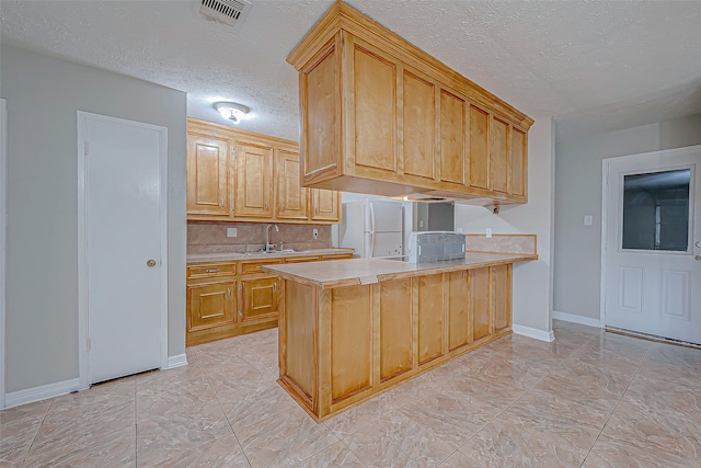 kitchen featuring white fridge, a textured ceiling, light brown cabinets, sink, and kitchen peninsula