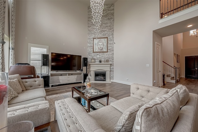 living room with a towering ceiling, a stone fireplace, and hardwood / wood-style flooring