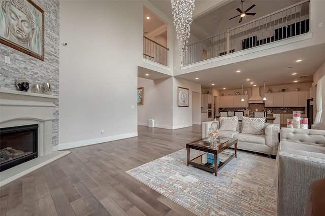 living room with a stone fireplace, hardwood / wood-style floors, ceiling fan, and a high ceiling