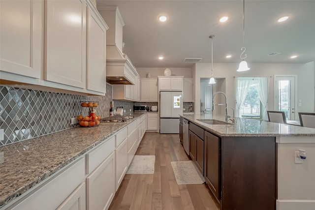 kitchen with light wood-type flooring, white cabinetry, sink, and a kitchen island with sink