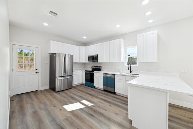 kitchen with kitchen peninsula, stainless steel appliances, sink, light hardwood / wood-style flooring, and white cabinets