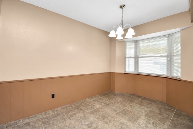 unfurnished room with wood walls and a notable chandelier